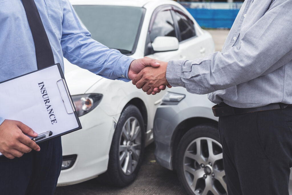 Insurance adjuster shaking hands with person in front of car crash scene. If you’ve been involved in a car accident, you need an insurance claims lawyer who will help you get the most out of your claim.