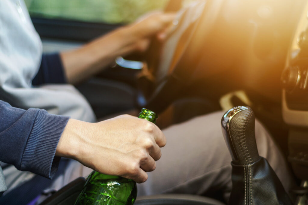 Close-up view of man holding a beer while driving. Our drunk driving accident lawyers can help you if you’ve been injured by an intoxicated driver. 