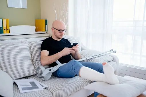 Man in a leg cast on the couch about to call his personal injury lawyer. Call a Car Accident Lawyer Expertise