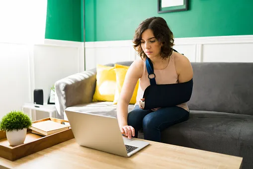 Woman in an arm brace as she sits on a couch and looks for a personal injury lawyer online.