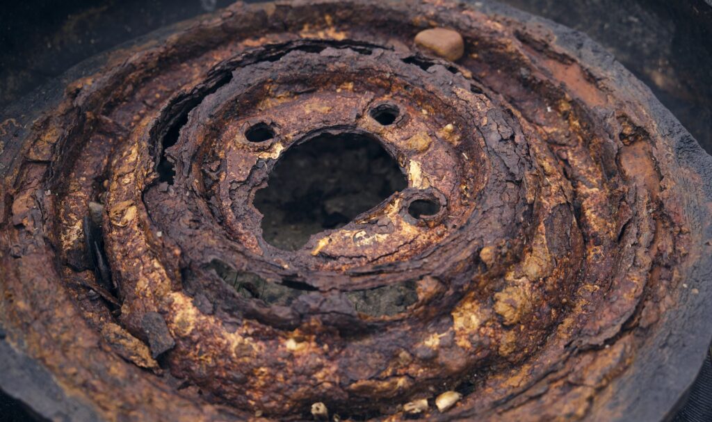 A photograph of a burned tire and rusted metal plates lying on the ground.