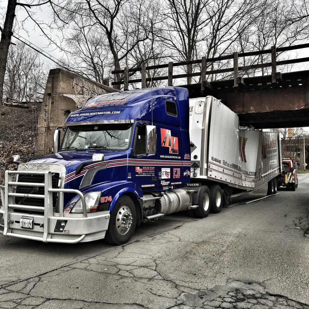 A large commercial truck stuck under a low-clearance bridge, illustrating the potential hazards and accidents associated with truck driving in urban areas