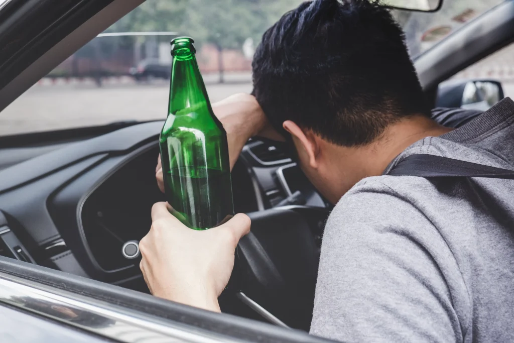 A driver holding a beer bottle.